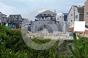 Tall unfinished cinder block foundation for a house being built near many older homes at the shore with a blank empty builders