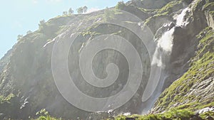 Tall waterfall in mountains, wind blowing water spray around