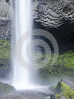 Tall waterfall into pool of water with rock overhang in background