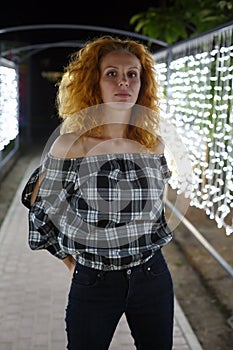 Tall, well-proportioned model-looking girl with red curly hair stands against the backdrop of glowing lights photo