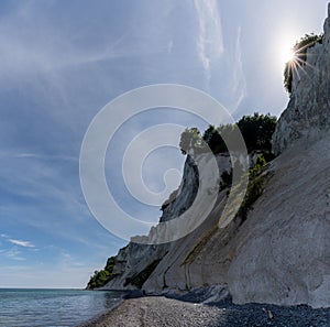 Tall white chalkstone cliffs and a rocky beach with calm ocean waters and a sun star photo