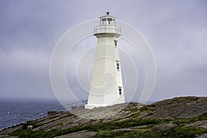 Tall white lighthouse overlooking the Atlantic Ocean during a foggy day along the East Coast Trail at Cape
