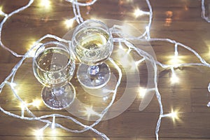 Tall wine glasses with bubbly drink for celebration toast wrapped in a Christmas light. Close up