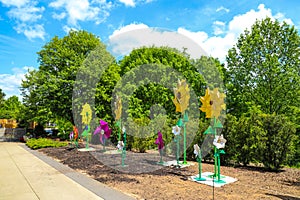 Tall yellow and green flower statues in the garden surrounded by colorful pinwheels and lush green trees and plants with blue sky