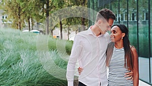 Tall young man kissing her african girlfriend while walking down the street