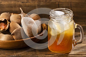 Tamarindus indica - Tamarind juice in a glass surrounded by fresh ripe tamarinds