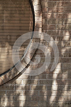 Tan brick wall with section of circular window covered by blinds