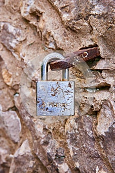 Tan rock wall, rusty metal loop, hook, rusting closed silver metal lock, background asset