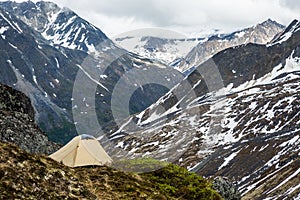 Tan tent on a narrow ledge overlooking broad valley and distance glaciers in the Talkeetna Mountains of Alaska