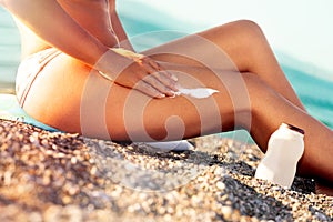 Tan woman applying sunscreen on legs