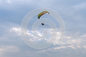 A tandem motor paraglider flies through the evening cloudy sky with a pilot and a passenger.