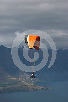 Tandem paraglider flying over lake in cloudy day