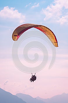Tandem paragliders flying in sunset over Interlaken in Switzerland. Silhouettes of Swiss Alps, pink sunset sky. Adventurous