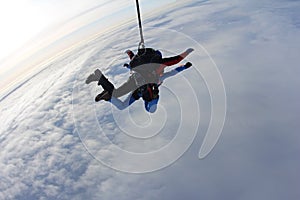 Tandem skydiving. Skydivers are flying above white clouds.