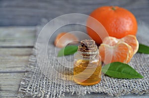 Tangerine essential oil in a glass bottle with fresh fruits on old wooden table.