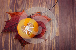 A tangerine with a heart cut in the skin lies on a dry autumn leaf on the table.