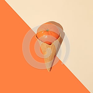 Tangerine in ice cream cone on orange and beige background. Minimal summer food concept. Flat lay