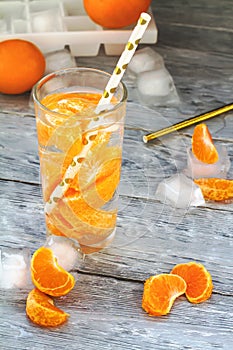 Tangerine,orange refreshing drink on a wooden table with scattered ice and slices of citrus fruit