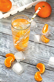 Tangerine,orange refreshing drink on a wooden table with scattered ice and slices of citrus fruit