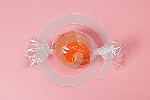 Tangerine wrapped like candy on bright pink background.