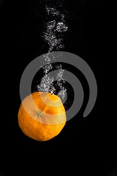 Tangerines drops in water with bubbles on a black background