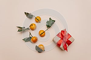 tangerines with green leaves lie on a beige pastel background next to a gift box tied with a red ribbon. Preparation for the new