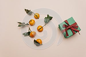 tangerines with green leaves, lying on a beige pastel background next to a green gift box.