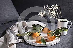 Tangerines with green leaves on white ceramic dish with a gray kitchen towel