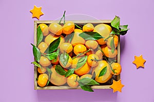 Tangerines with leaves in a box on a lilac background