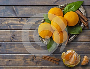 Tangerines with leaves and cinnamon stick on a silver or metal tray or platter on a dark wooden table. The view from the top