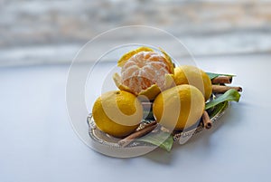 Tangerines with leaves and cinnamon stick on a silver or metal tray or platter on a light table