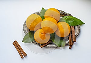 Tangerines with leaves and cinnamon stick on a silver or metal tray or platter on a light table. The view from the top