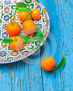Tangerines with leaves in plate on wooden background, in blue