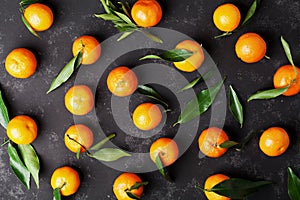 Tangerines or mandarins with green leaves on vintage black table from above in flat lay style.
