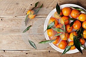 Tangerines or mandarins with green leaves on vintage wooden table from above in flat lay style.