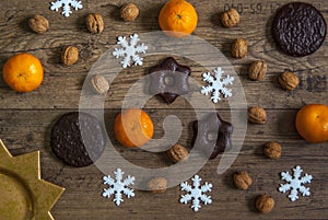 Tangerines, nuts, gingerbread and spiced biscuits, star-like snowflakes, sun disordered on rustic wooden floor background