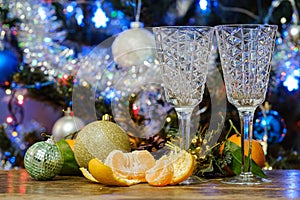 tangerines and two champagne glasses on the table against the background of a Christmas tree
