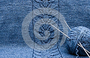 A tangle of blue grey wool yarn with knitting needles on knitted cloth with a pattern