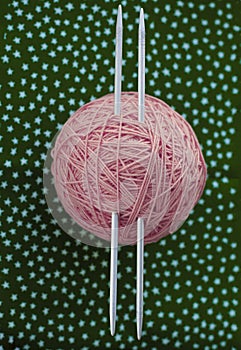 Tangle of pink threads and knitting needles lie  a dark green background