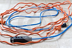 Tangled blue and orange extension cords on white background