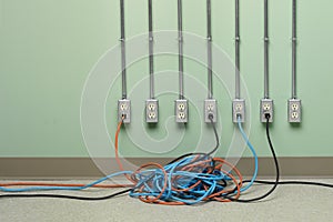 Tangled extension cords plugged into row of AC electrical outlets