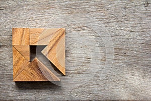 Tangram puzzle as arrow in square shape on wood background photo