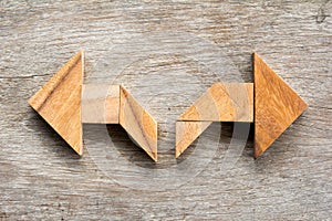 Tangram puzzle as two way arrow shape on wood background