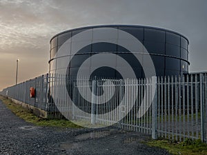 Tank for diesel or petrol fuel storage behind metal security fence at sunset. Oil industry supply chain. Protection of asset