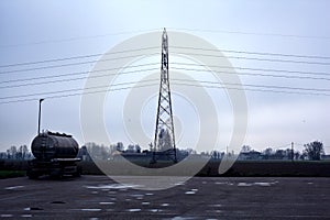 Tank in a parking lot by the edge of a fields with a pylon on a cloudy day