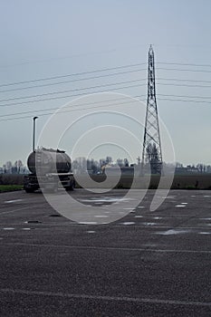 Tank in a parking lot by the edge of a fields with a pylon on a cloudy day