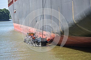 Tanker boat or bunker barge at the hull of a large container freighter takes over oily residues and sanitary wastewater in the