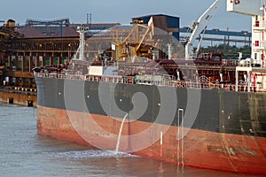 Tanker discharging cooling water water in harbor waters at evening time