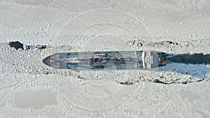 A tanker is moving along a channel among the endless ice. Drone view