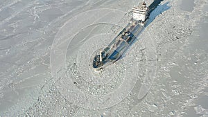 A tanker is moving along a channel among the endless ice. Drone view